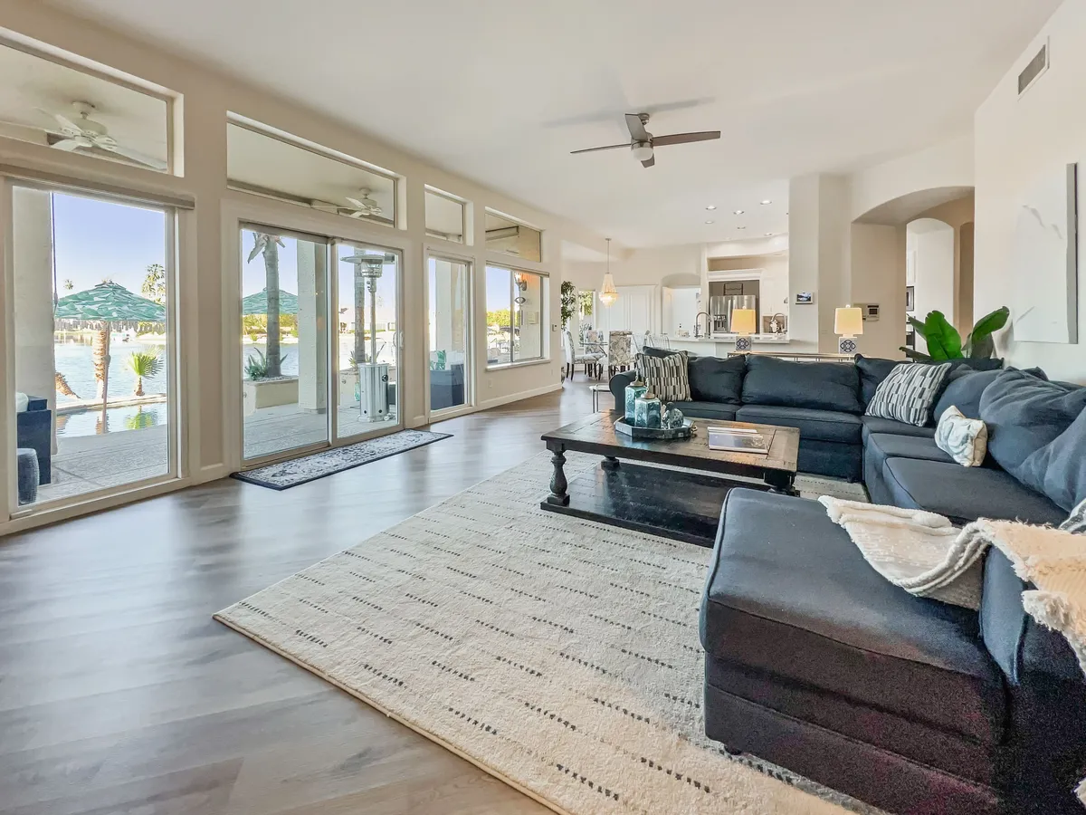 A cozy, inviting living room with a large sectional sofa, a coffee table, and expansive windows offering a direct view of the water. Decorative plants bring in a touch of nature, while the space is arranged for socializing and taking in the scenic lakeside views.