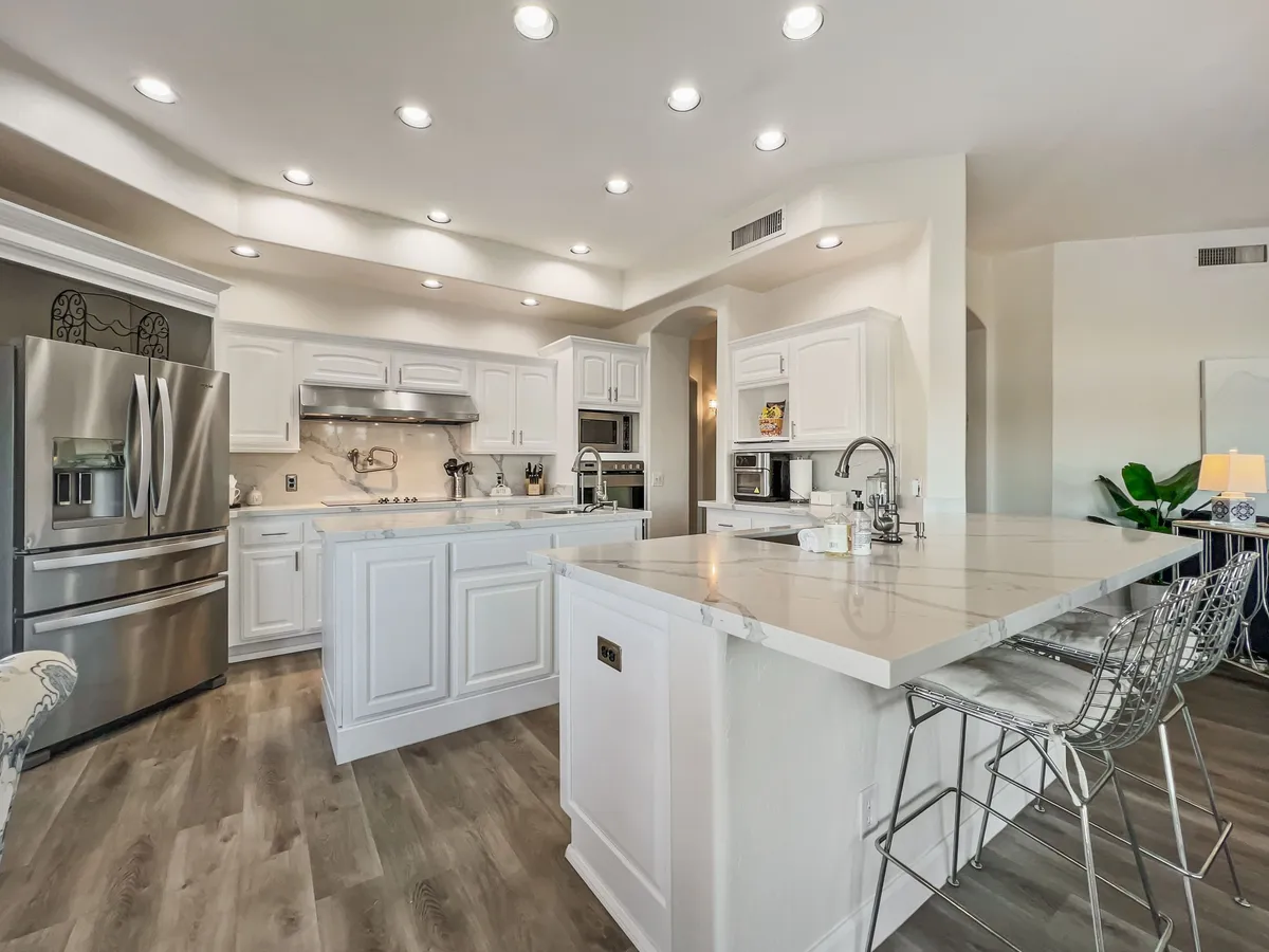 This bright, cheerful kitchen features a spacious kitchen island with bar stools, stainless steel appliances, and white cabinetry. The island serves as a breakfast bar, and the open layout is perfect for both cooking and entertaining. Natural light pours into the space, highlighting the modern finishes and ample countertops.