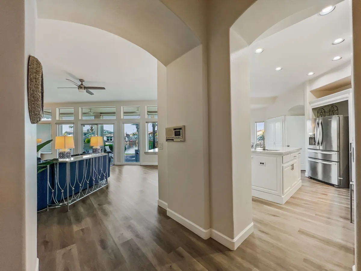 A modern, light-filled kitchen and living area with a central island, blue bar area, and large windows overlooking the outdoors. The open-concept layout is perfect for cooking together, hosting movie nights, or enjoying sunset views from inside.