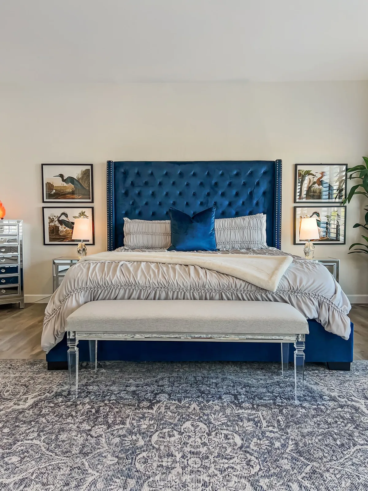 A serene bedroom with a blue upholstered headboard, plush bedding, decorative pillows, tasteful artwork, and mirrored furniture. The mood is both luxurious and tranquil, perfect for illustrating another of the king suites or secondary bedrooms.