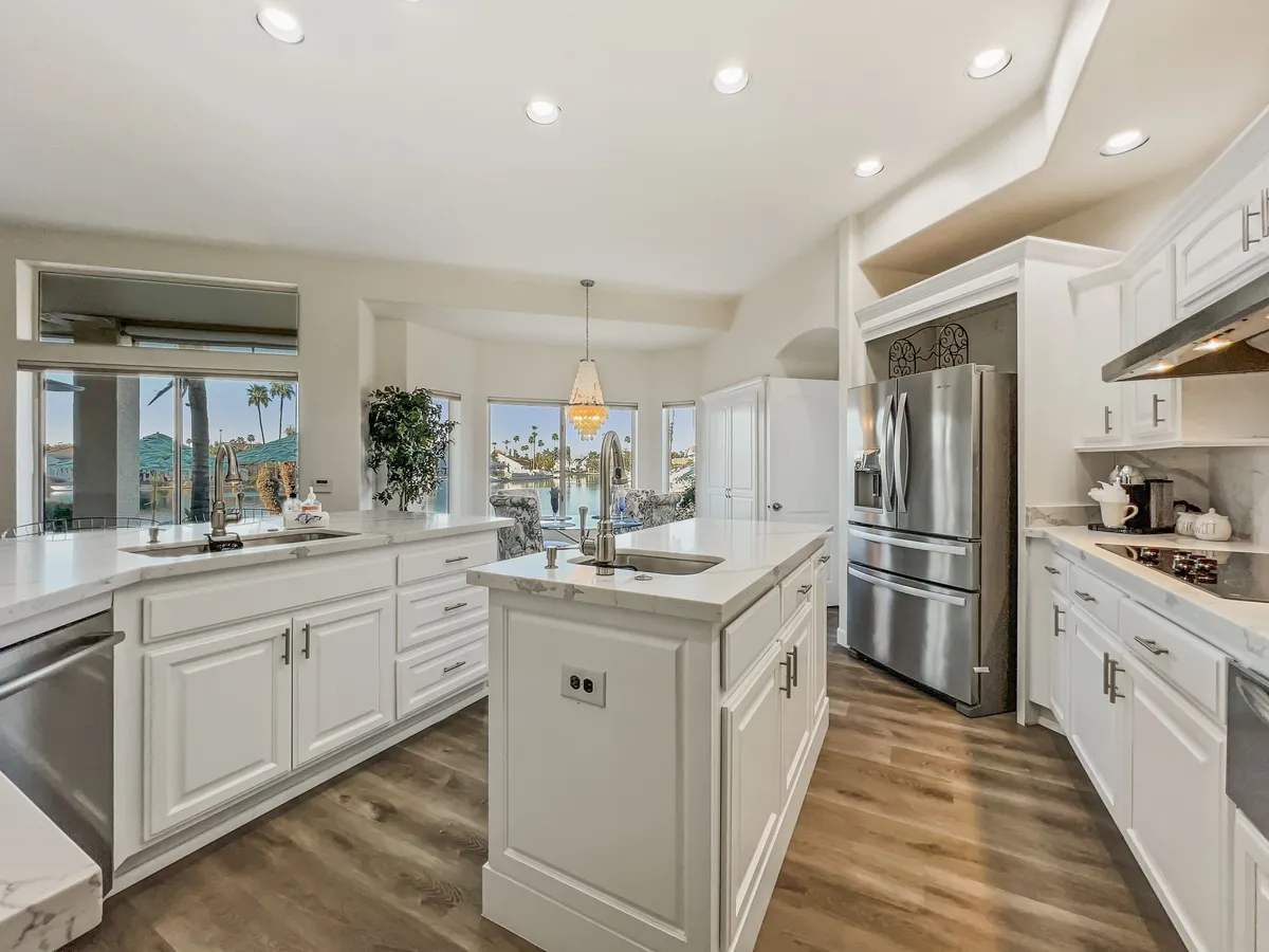 The kitchen is bathed in warm light from large windows, with a spacious island, stainless steel appliances, and comfortable bar seating. The view through the windows hints at scenic surroundings, likely the lake, further connecting the space to the described breakfast nook and morning rituals.