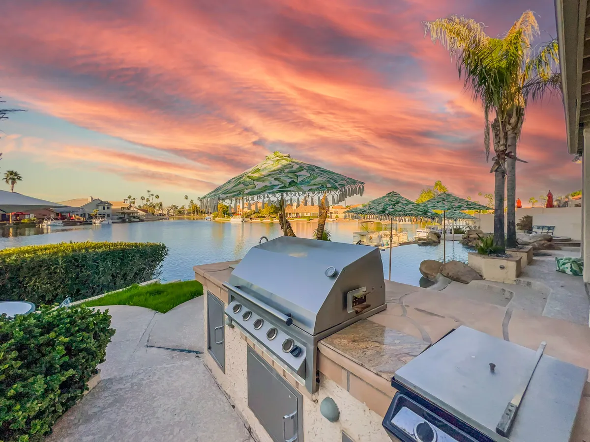 This exterior image spotlights an outdoor kitchen and grill setup with umbrella-covered seating, positioned right by the water for memorable alfresco dining experiences.