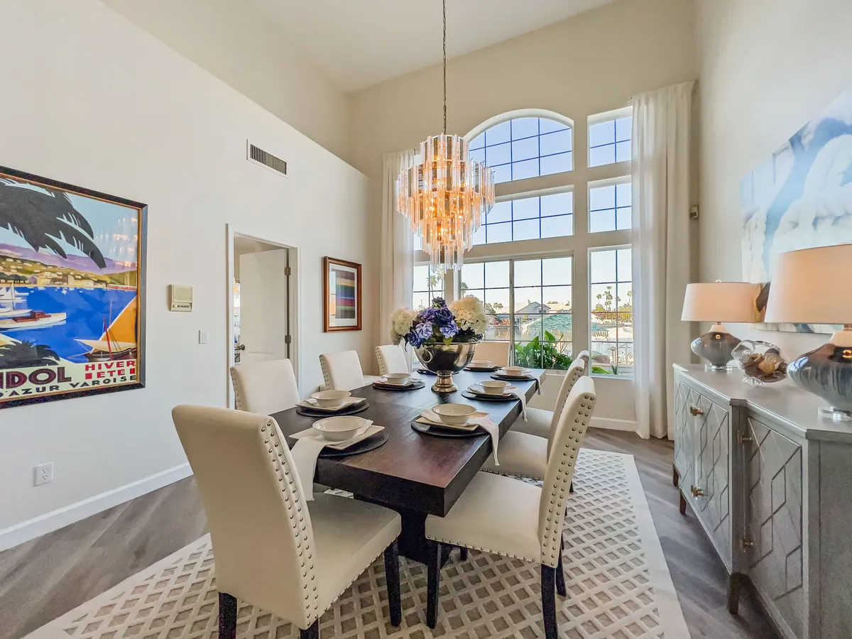 An elegant formal dining room illuminated by a chandelier, featuring a generously sized dining table set near large windows and contemporary artwork, setting the stage for memorable meals and gatherings.